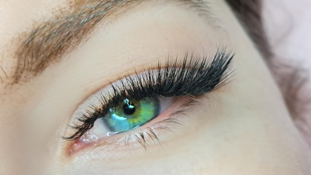 A woman with bright blue and slightly green/turquoise eyes with Cat eye styled lash extensions. The Cat eye eyelash extensions become thicker towards the outside of the eye.