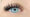 A woman with bright blue eyes and a Doll style lash extension. The doll style eyelash extension is thick and becomes thicker and longer towards the outside of her eye.