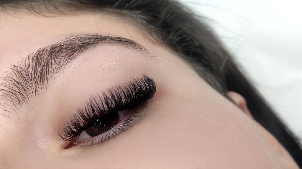 A woman with very dark brown eyes and thick Russian volume eyelash extensions. The make up is very minimal and natural with some pink eyeshadow on the top eyelid. This enhances the Russian volume lash extensions so they look very full.