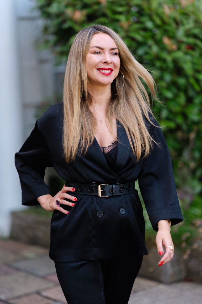 Edy London wearing a black jacket, trousers and belt outside.