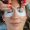 A lady having eyelash extensions put on using tweezers by a woman with red nails.